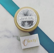 Load image into Gallery viewer, Handcrafted candle jar labeled &#39;Sleigh Ride&#39; with a decorative ribbon on a marble surface.
